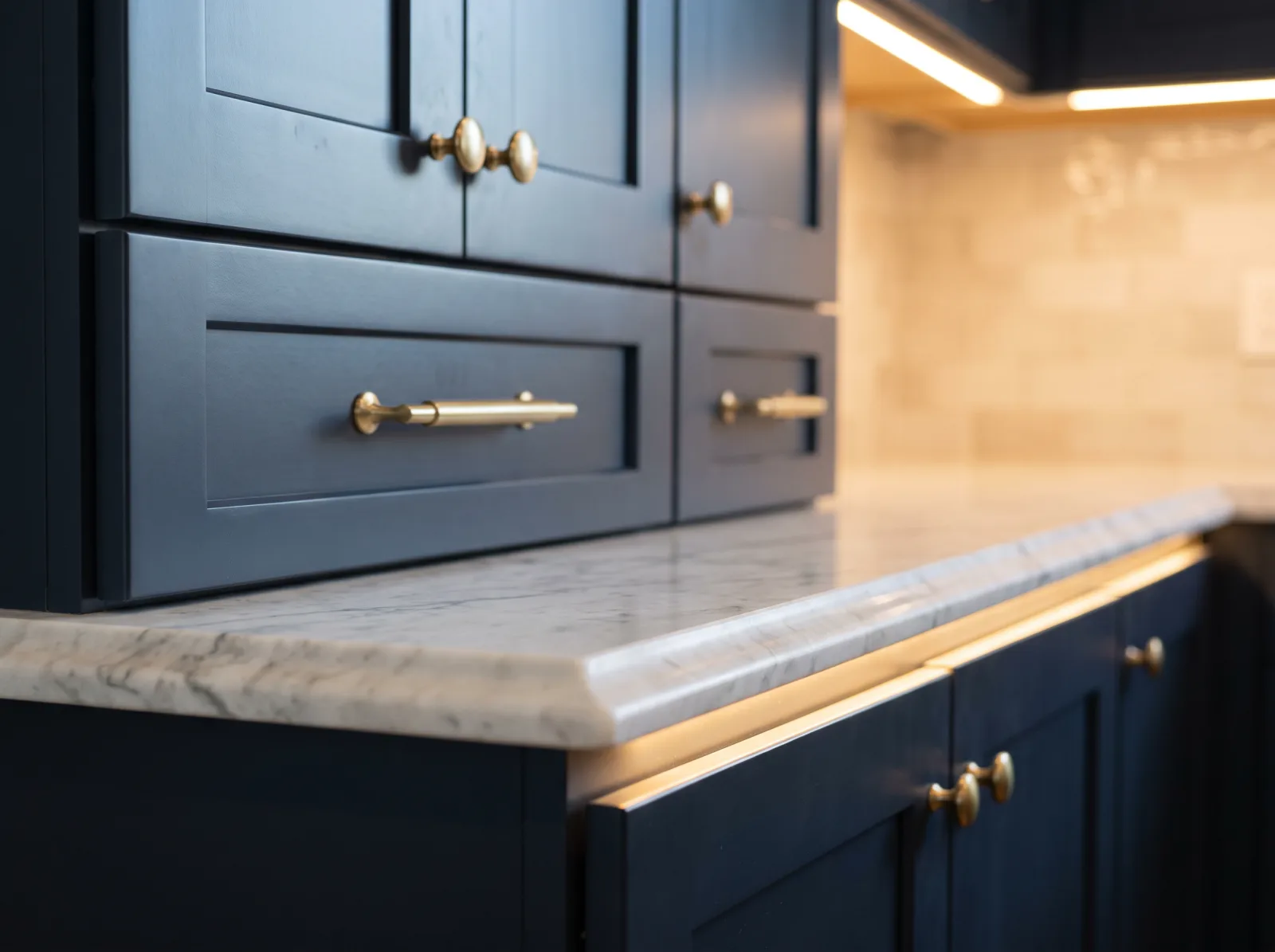 Detail of navy shaker cabinetry with brushed brass hardware and marble countertop edge